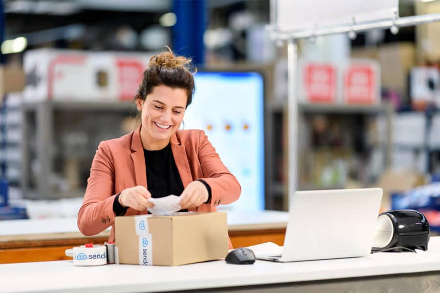 Person mit Etikettendrucker bringt Etikett an einem Paket an