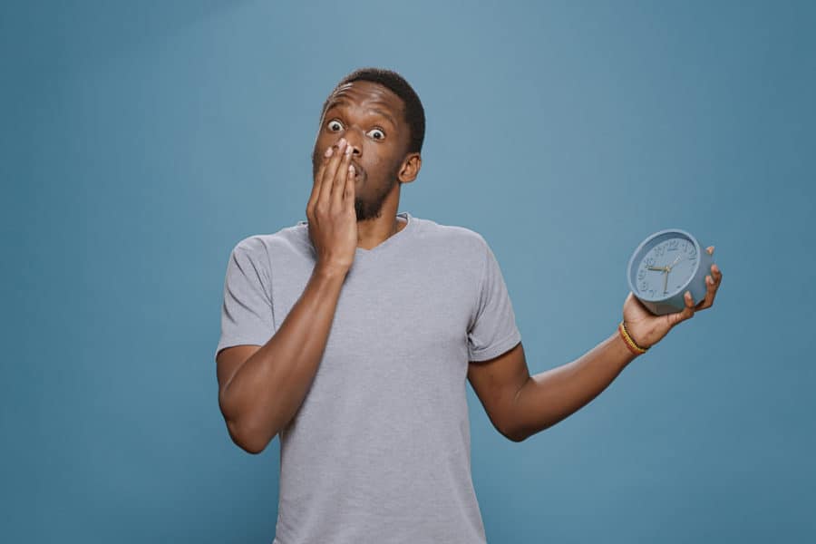 Shocked man with clock waiting for delivery due to shipping delays.