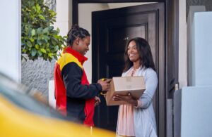 DHL Chauffeur bei der Haustürzustellung mit einer Empfängerin bei der Übergabe des Paketes