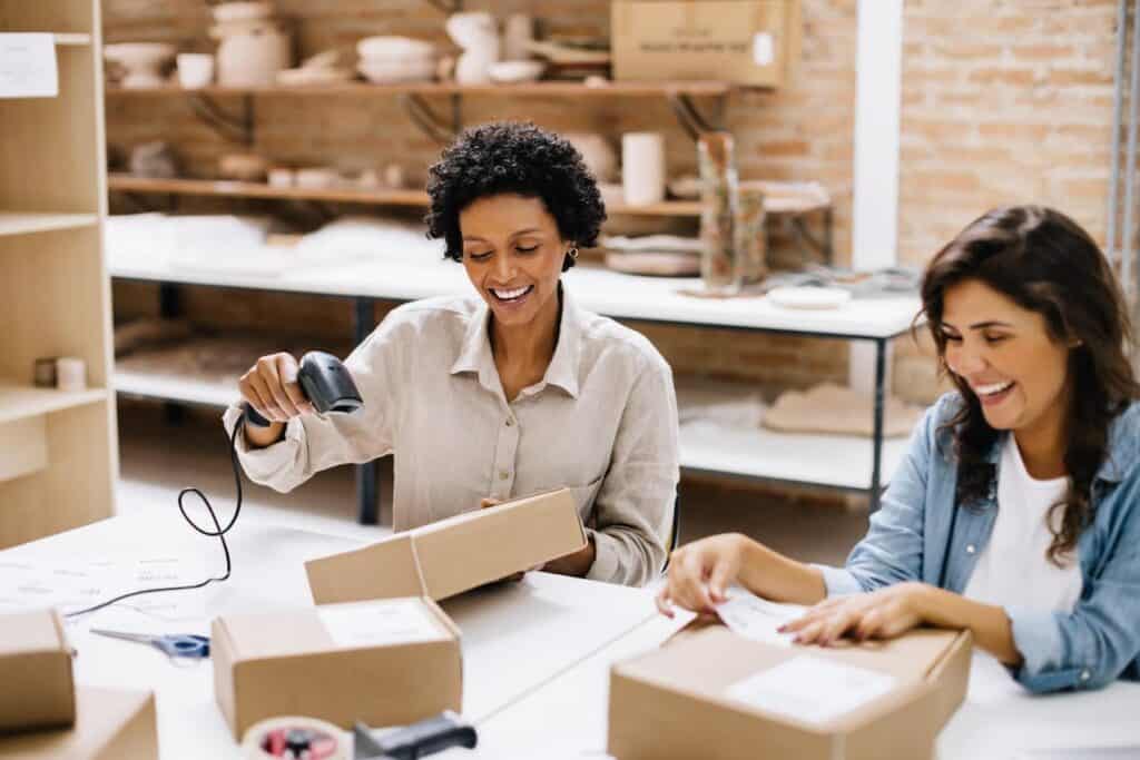 Zwei Frauen packen Retouren im Onlinehandel in Pakete und kleben Versandlabel drauf