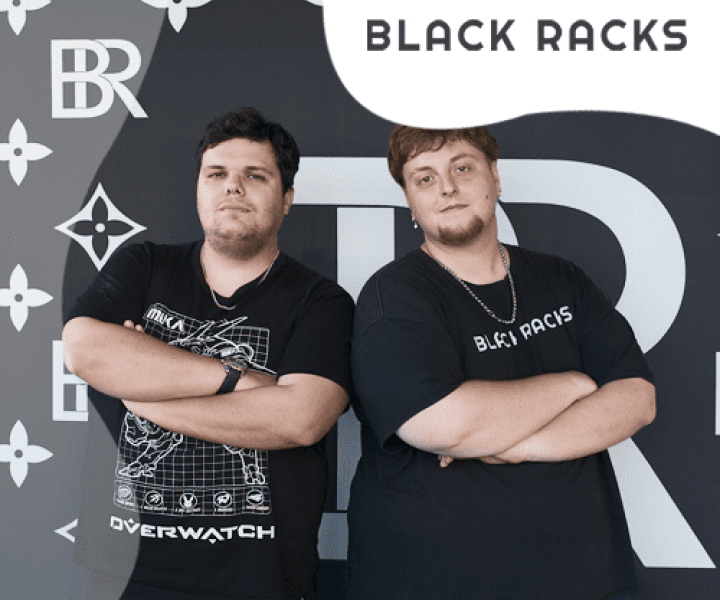 Two individuals with crossed arms wearing black t-shirts, standing in front of a "BLACK RACKS" sign.