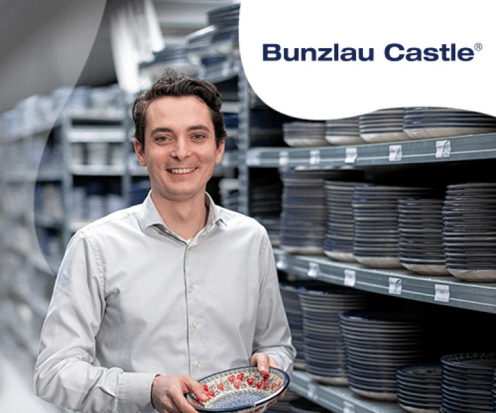 Person holding a ceramic dish in a warehouse with stacks of plates. "Bunzlau Castle" logo visible.