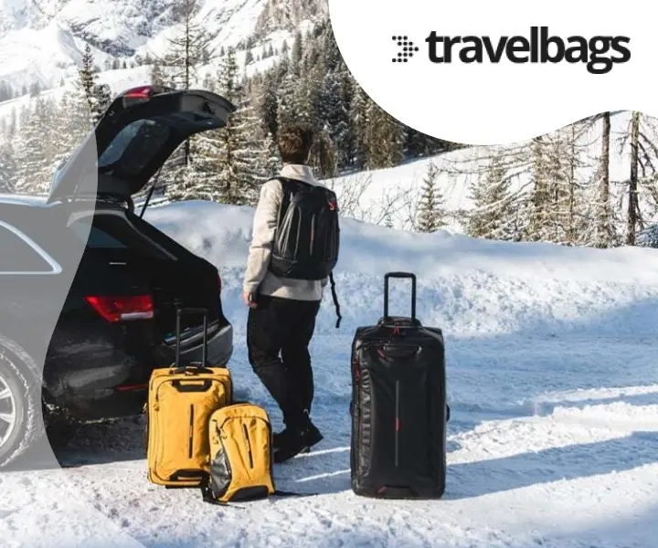 Person with travel bags standing next to a car in a snowy mountain landscape, with the Travelbags logo.