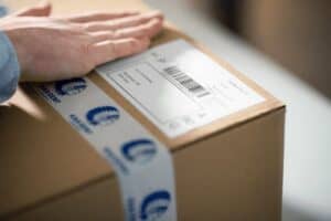 Imagen de una mano cerrando una caja de KAA Gent tras calcular los gastos de envío.